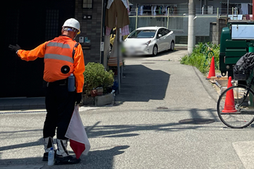 平野区の重機備え付けによる荷上げ作業現場で交通誘導警備をする警備員2(2025.06.28)