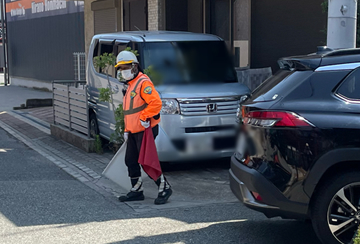 平野区の重機備え付けによる荷上げ作業現場で通行者保全をする警備員(2025.06.28)
